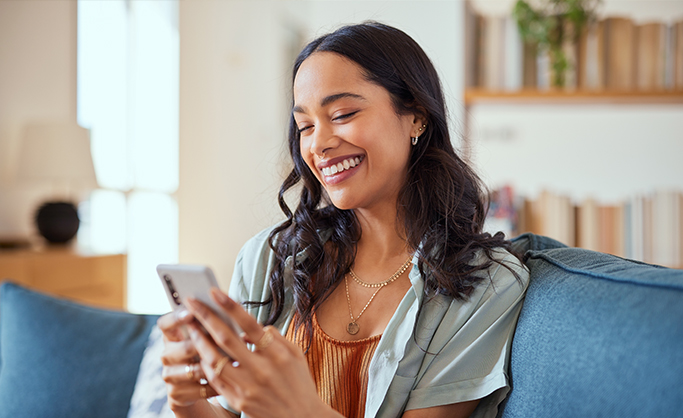 A young woman smiling at her phone while reading about credit union myths.